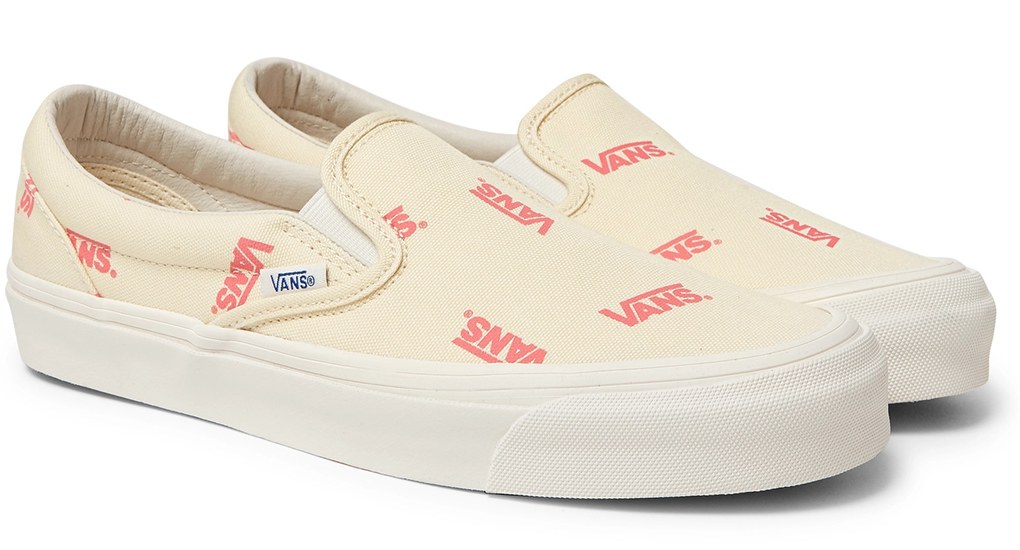 Vita slip-ons från Vans med röda logotyper som tryck.